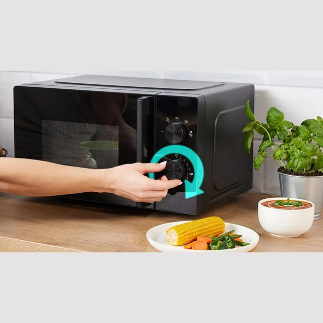 Рука поворачивает регулятор чёрной микроволновой печи Gorenje